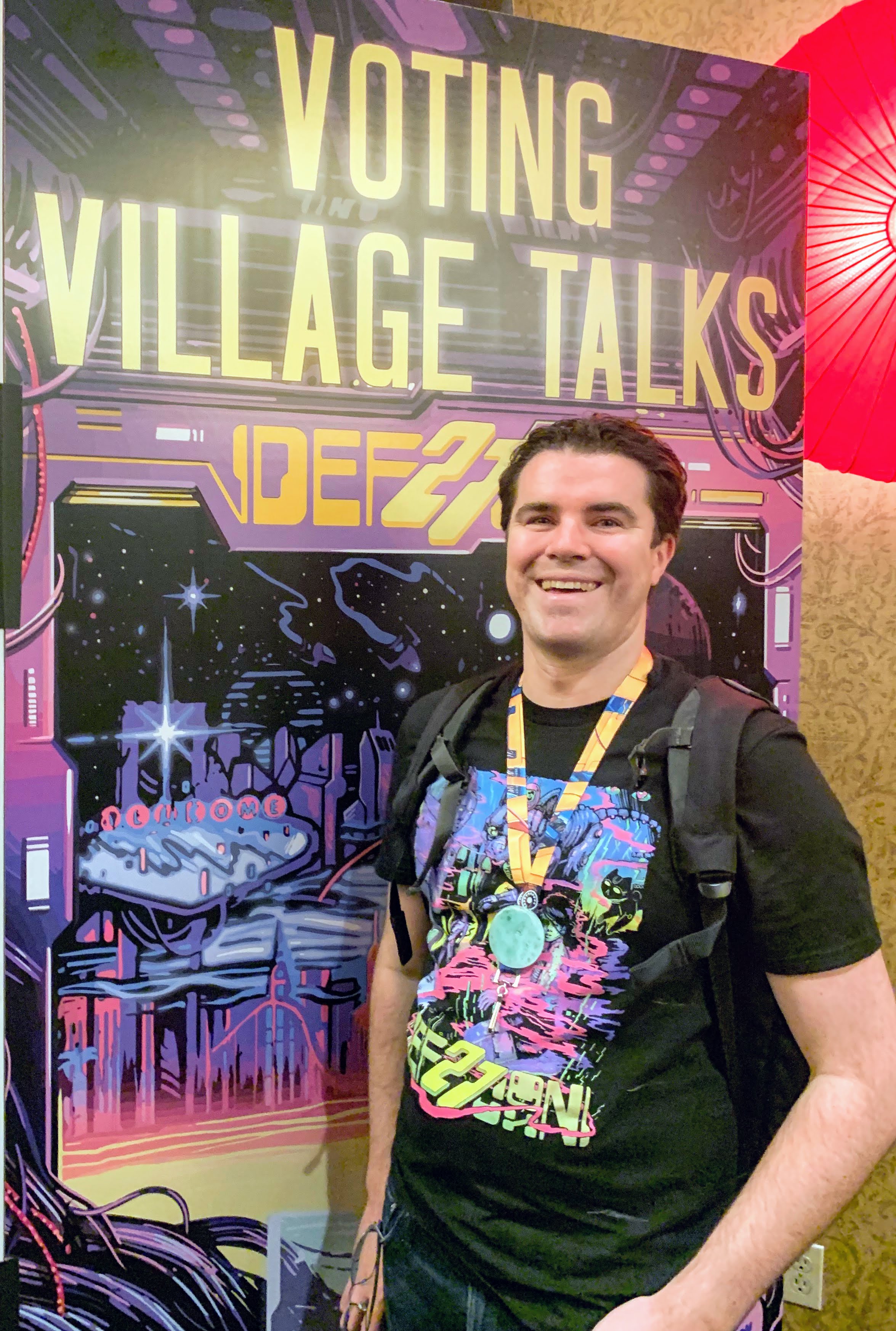 Tim Watts stands beside Def Con poster.